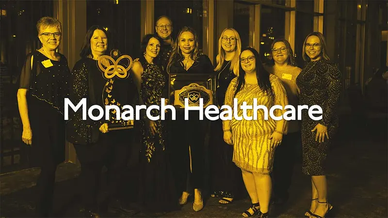 A group on a red carpet in front of a Monarch Healthcare backdrop, from their staff appreciation event